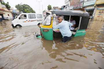 An Indian man pushes an autorickshaw past a flooded street after heavy rainfall in Ahmadabad, India on Friday.