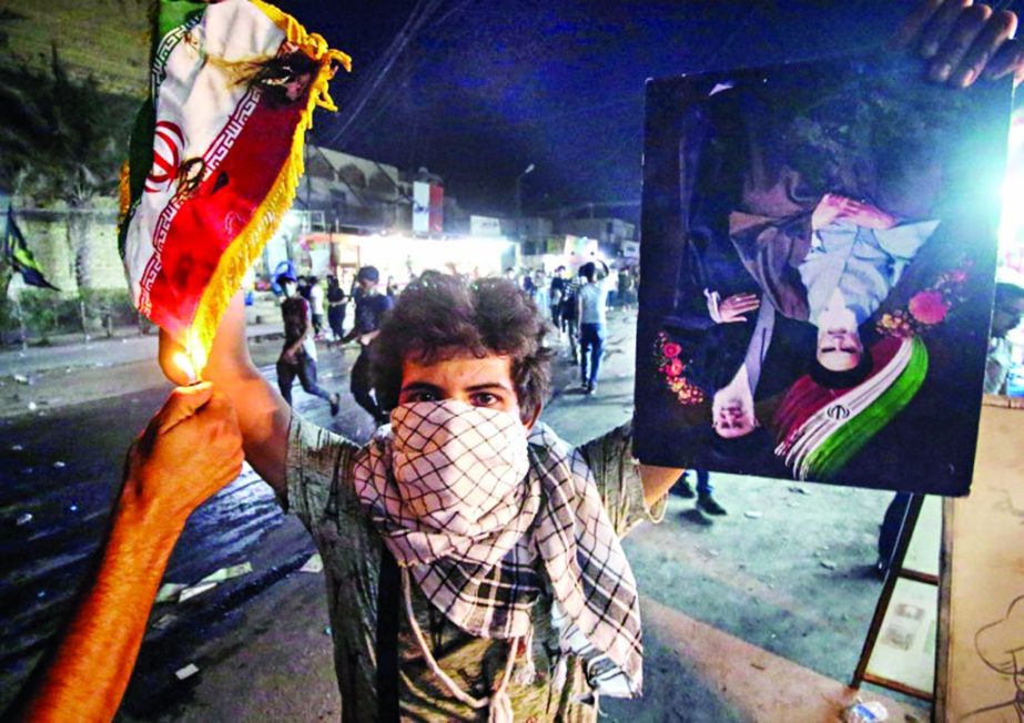 An Iraqi protester holds up an Iranian flag as another one sets it on fire for and an upside down picture of Iranian leaders after demonstrators set on fire the Iranian consulate in the southern Iraqi city of Basra.