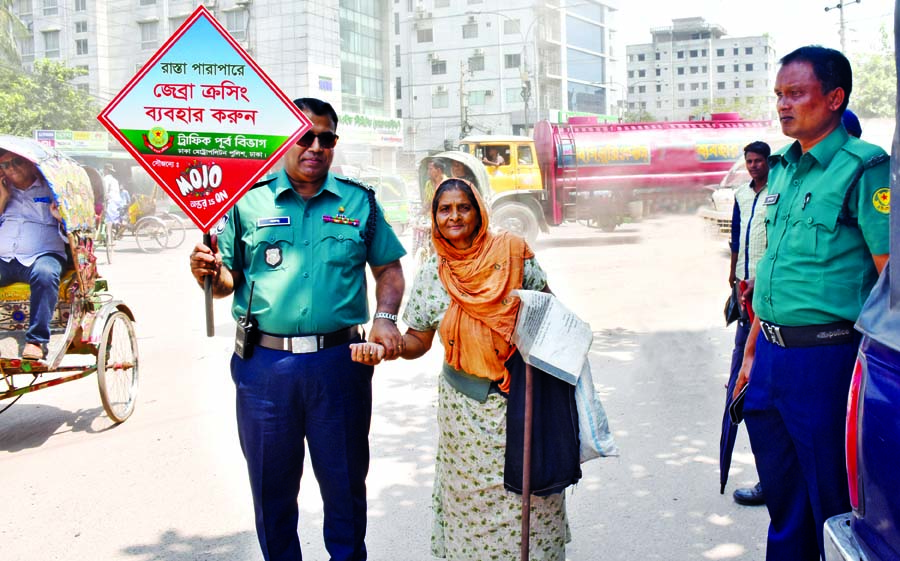 A police man carrying a placard on road safety awareness helping an old woman to pass the road near Dayaganj's Chowrasta area on Monday.