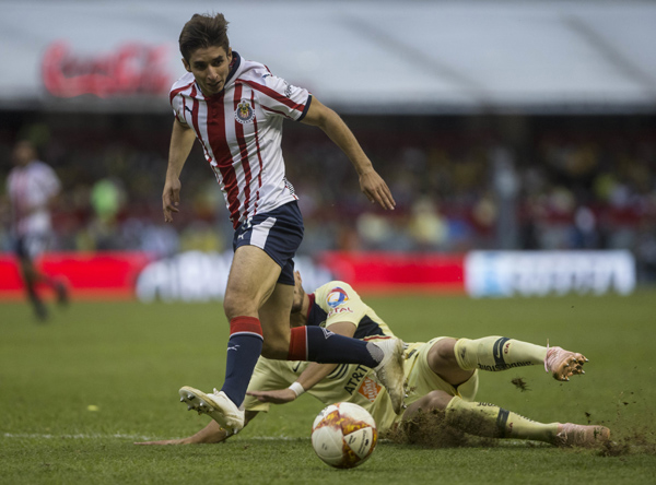 America's Matheus Uribe falls as he fights for the ball with Chivas' Isaac Brizuela during a local soccer league match in Mexico City on Sunday.