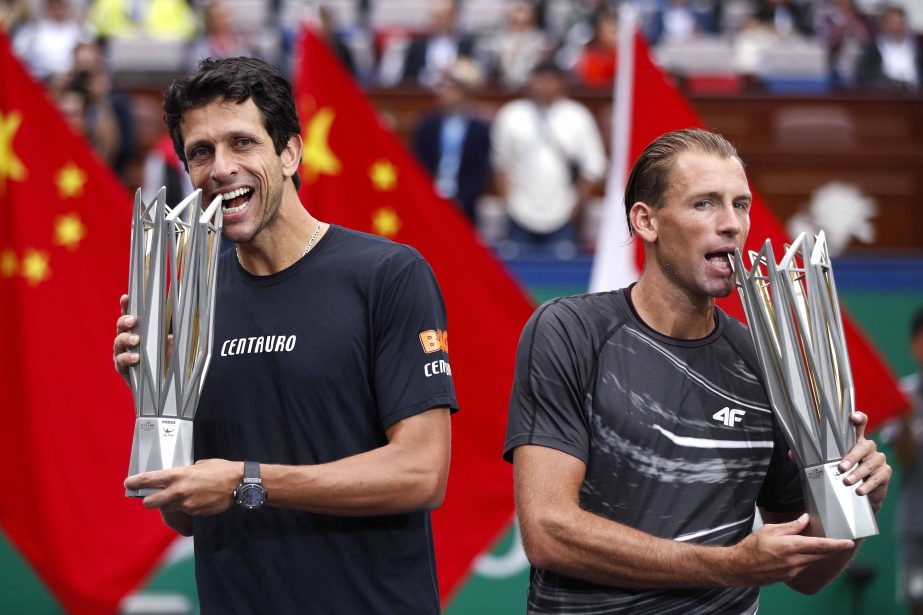 Marcelo Melo of Brazil (left) and his partner Lukasz Kubot of Poland bite their winning trophy as they pose for photographers after beating Jamie Murray of Britain and Bruno Shares of Brazil in the men's doubles final match of the Shanghai Masters tennis