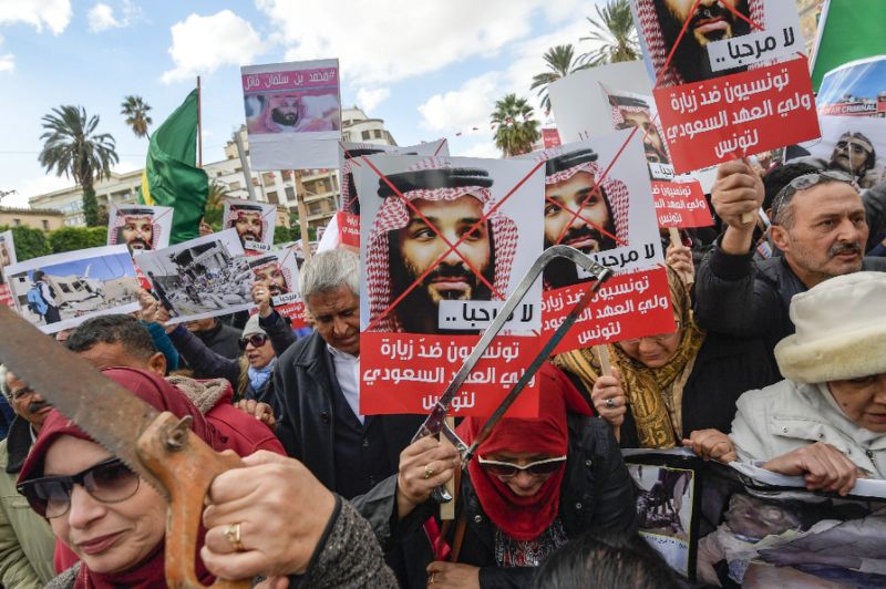 Tunisian women hold up saws and signs showing pictures of Saudi Crown Prince Mohammed bin Salman with a caption below reading in Arabic "no welcome, Tunisians against the visit of the Saudi Crown Prince to Tunisia"