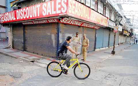 A man pedals his bicycle past police officers standing in front of the closed shops during a strike called by Hindu nationalist Bharatiya Janata Party (BJP) and Rashtriya Swayamsevak Sangh (RSS) to protest against state government for allowing two women t