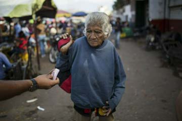 An elderly woman is offered cash as she begs at a wholesale food market in Caracas on Monday. Economists agree that the longer the standoff between the U.S.-backed opposition leader Juan Guaido and President Nicolas Maduro drags on, the more regular Vene