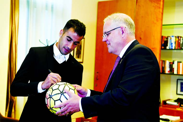 Refugee Hakeem al-Araibi (left) signs a ball for Australian Prime Minister Scott Morrison at Parliament House in Canberra, Australia on Thursday. Al-Araibi was detained in Thailand for three months under threat of extradition to Bahrain and has come to Ca