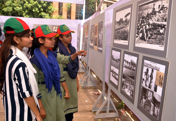 Visitors coming from different schools see the photographs of the Liberation War organised on the occasion of Liberation War Festival-2019 by the National Museum at the playground of Dhaka University on Friday.