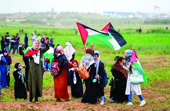 Palestinian women protesters flash the victory sign and wave Palestinian flags during a demonstration marking the first anniversary of the "March of Return" protests, near the border with Israel east of Gaza City.