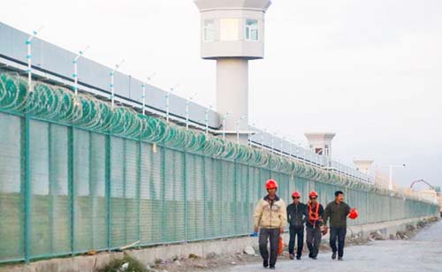 Workers walk by the perimeter fence of what is officially known as a vocational skills education centre in Dabancheng in Xinjiang Uighur Autonomous Region, China.