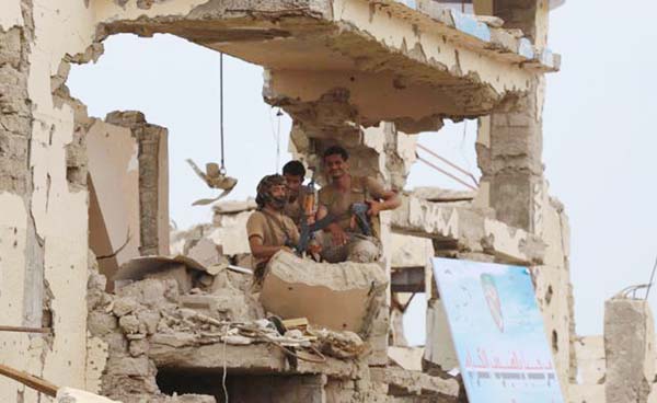 Saudi-backed Yemeni fighters watch from a destroyed building the launch ceremony by Saudi Development and Reconstruction Program for Yemen (SDRPY) of multi-million dollar aid projects in the area of Yemen's northern coastal town of Midi, located in confl