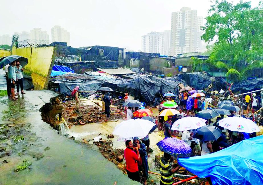 People stand among the debris after a wall collpased on hutments due to heavy rains in Mumbai, India on Tuesday.