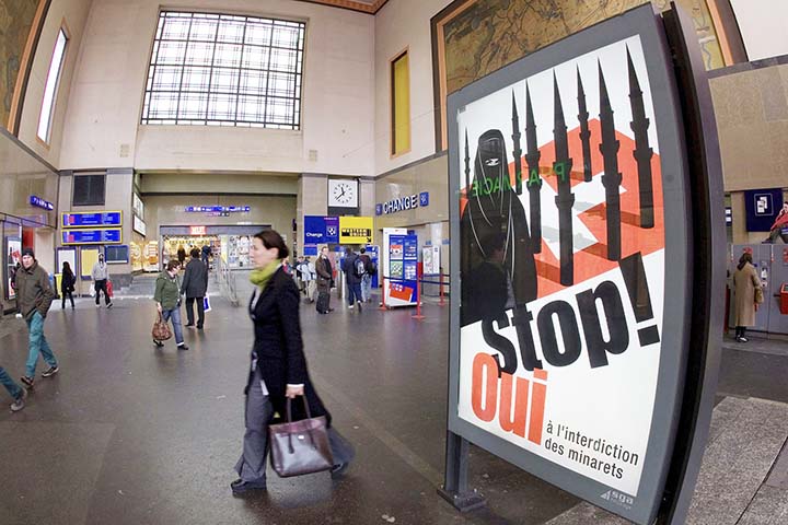 People walk by a poster from the right-wing Swiss People's Party (SVPUDC) depicting a woman wearing a burqa in front of a Swiss flag upon which are minarets which resemble missiles, at the central station in Geneva, Switzerland. Later in the month, a su