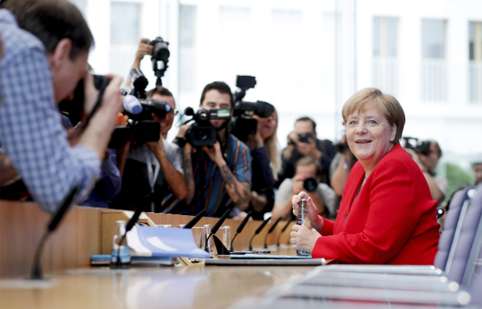 German Chancellor Angela Merkel, right, smiles as she arrives for her annual sommer press conference in Berlin, Germany on Friday.