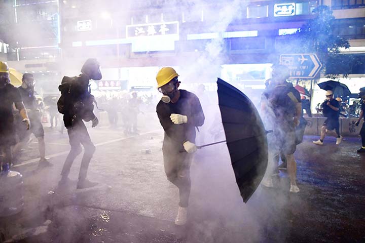 Hong Kong protesters are enveloped by tear gas fired by police.