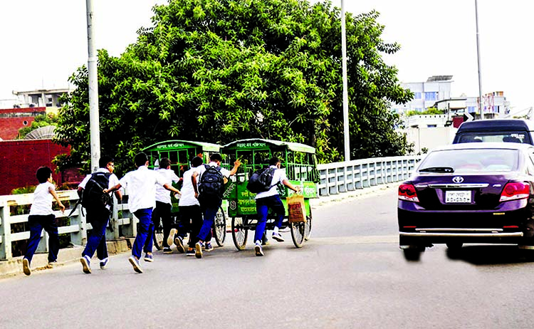 Some students pushing their school vans on Dhaka's first U-loop at Rampura in a bid to avoid traffic jam despite ban on plying non-motorised vehicles on it.