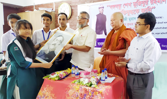 Freedom Fighter Kazi Murad Hossen presents a picture of Bangabandhu to a student of Banophool Adibashi Green Heart College at a programme on Bangabandhu and Liberation War of Bangladesh held at the college campus recently.