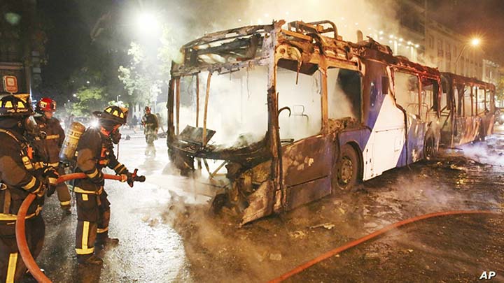 Firefighters put out the flames on a burning bus during a protest against the rising cost of subway and bus fares, in Santiago, Chile on Friday.