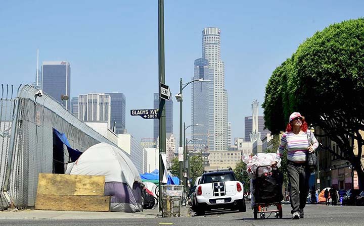 A woman pushes a cart full of her belongings past tents near Skid Row in downtown Los Angeles.