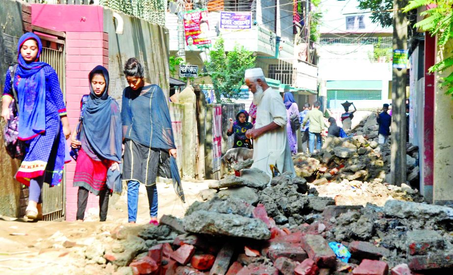 Pedestrians walk past heaps of earth and a trench dug by Dhaka South City Corporation for installation of sewerage pipes on Mothertek Road in the city on Friday. The residents of the area are facing immense sufferings due to the road excavation.
