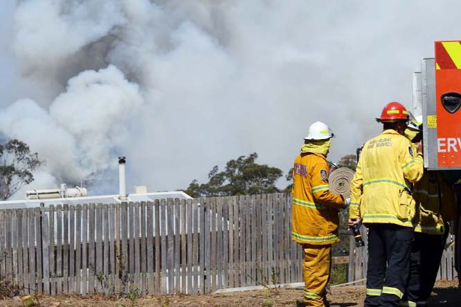 Firefighters work to protect a home as smoke from bush fires rises Friday in Penrose, Australia.