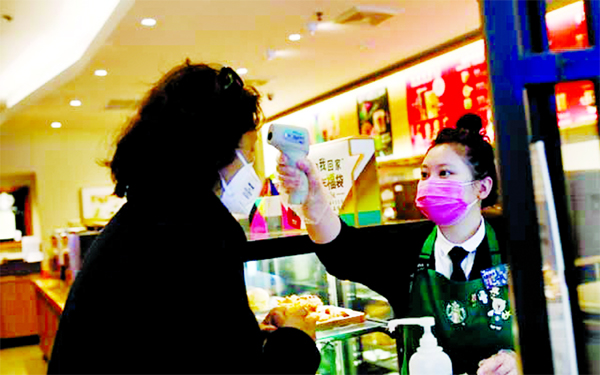 A worker uses a thermometer to check the temperature of a customer as she enters a Starbucks shop as the country is hit by an outbreak of the new coronavirus, in Beijing, China.