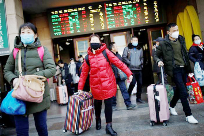People wearing face masks carry their luggage as they walk outside Beijing Railway Station as the country is hit by an outbreak of the new coronavirus, in Beijing.