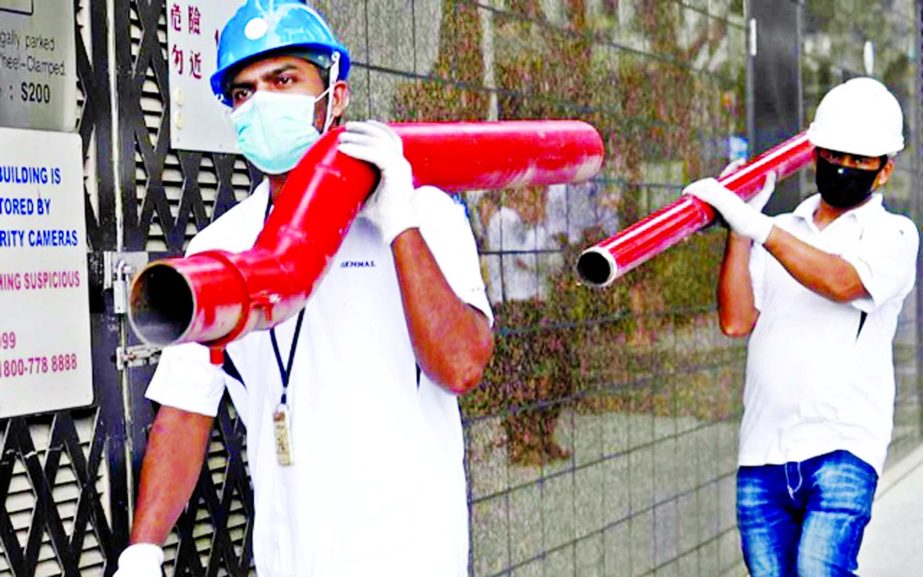 Construction workers wearing masks in precaution of the coronavirus outbreak carry pipes as they pass a building in the Central Business District in Singapore.