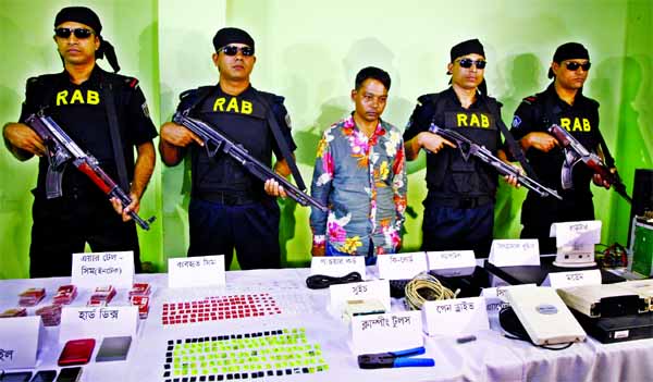 RAB personnel produce Sohel Ahmed, an accused ringleader of mobile banking forgery, before media on Friday after his arrest from the city's Mirpur area of Thursday night. A laptop, a multi-SIM gateway, a signal booster, three modems and a large number of