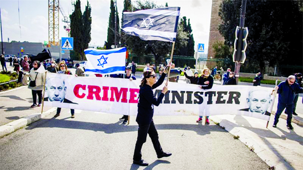 People wave Israeli flags and carry a banner reading 'crime minister' during a protest outside the Israeli parliament in Jerusalem.