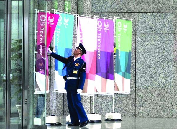 A guard straightens a banner promoting the Tokyo 2020 Olympics in Tokyo on Monday. The IOC will take up to four weeks to consider postponing the Tokyo Olympics amid mounting criticism of its handling of the coronavirus crisis that now includes Canada say