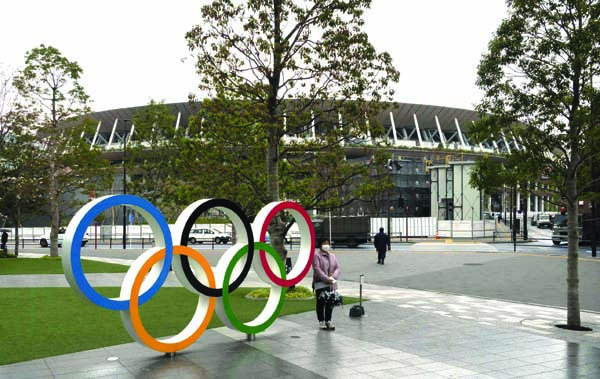 A woman poses for photo next to the Olympic rings near the New National Stadium in Tokyo on Monday.