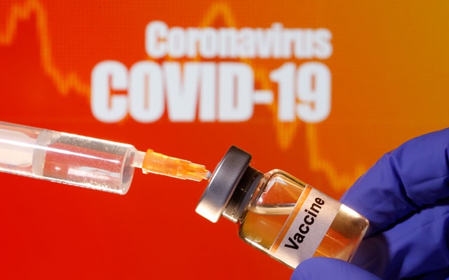 A small bottle labelled with a "Vaccine" sticker is held near a medical syringe in front of displayed ``Coronavirus COVID-19`` words in this illustration taken Apr 10, 2020. REUTERS