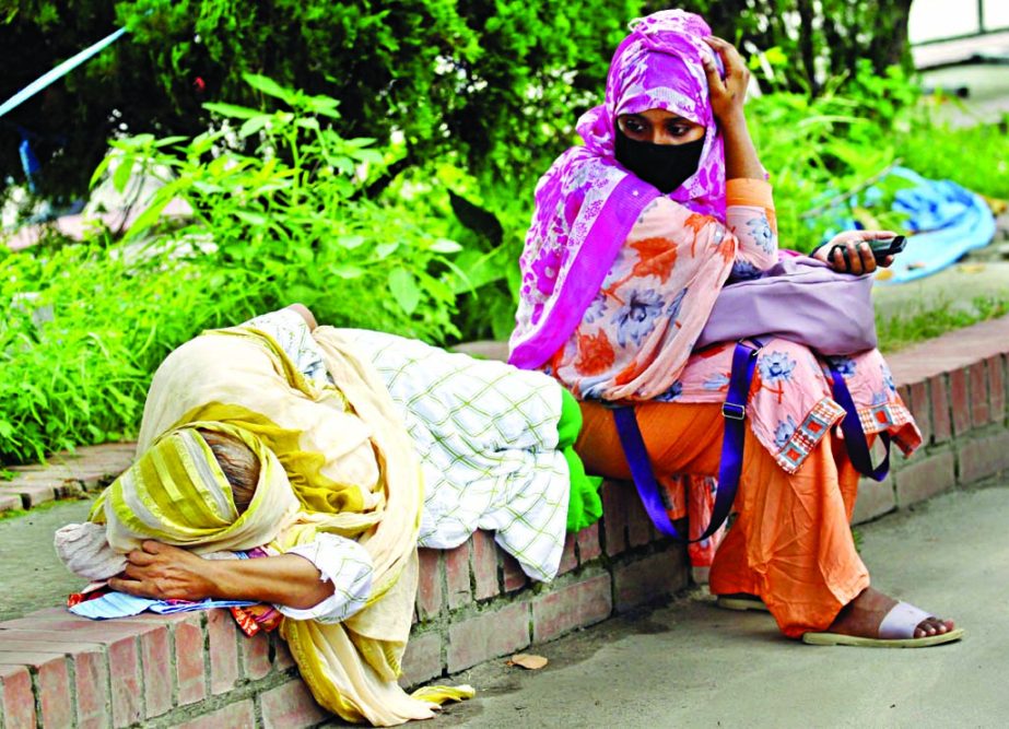 An elderly woman lays down on a wall after long wait to give her swab sample to be tested for Covid-19 at Mugda General Hospital in the capital on Monday, while her daughter looks at her with an anxious face.