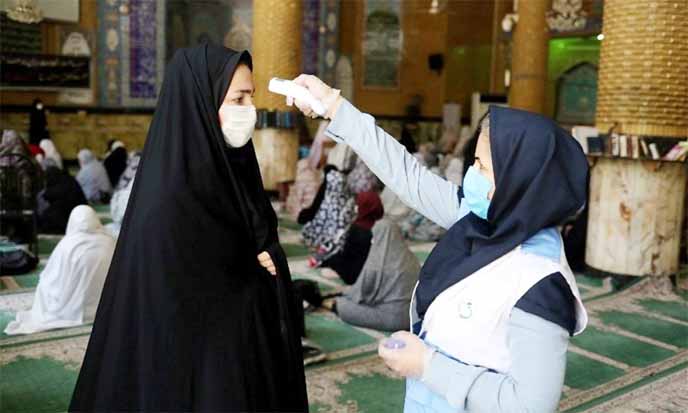 In this file photo, an Iranian woman wearing a protective face mask checks the temperature of a worshipper before attending the Friday prayers in Qarchak Jamee Mosque.