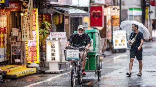 A deliveryman partially wears a face mask as he cycles in the rain in Tokyo on Tuesday. Internet