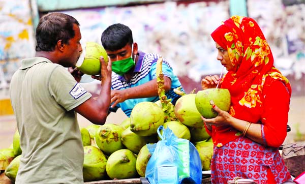Exhausted by the scorching summer heat, thirsty pedestrians take green coconut water at Paltan area in the capital on Friday.