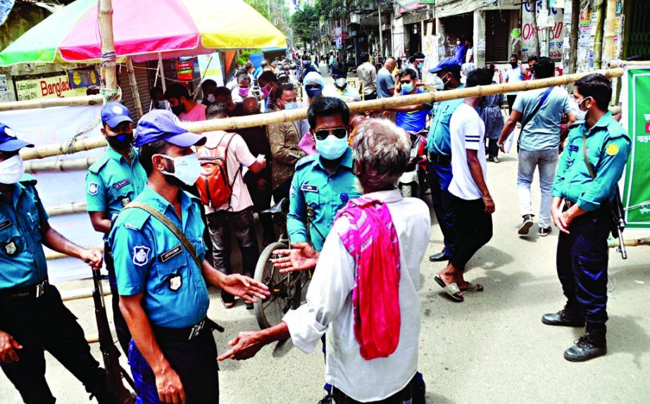 A man is being restricted by police personnel while passing through bamboo-made barricades in Dhaka's Wari on Saturday as the authorities have enforced a three-week lockdown there to contain the spread of coronavirus.