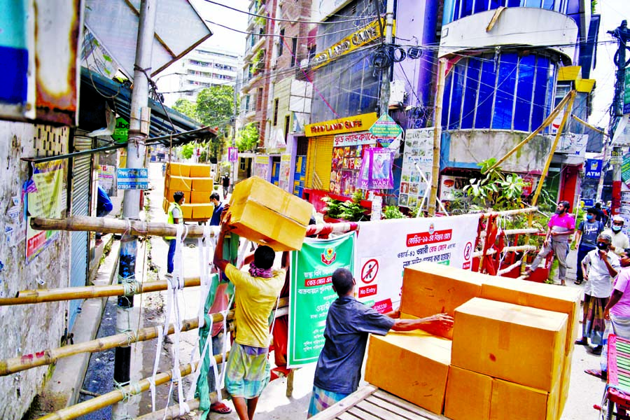 Labourers of a business house transporting box cartons defying bamboo that erected to control illegally movement of people during ongoing lockdoon in the city's Wari. The photo was taken from Post Office Lane on Monday.