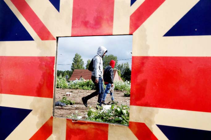 Migrants are reflected in a mirror bordered with the Union Jack as French police officers dismantle a makeshift shelter camp in Calais, France on Friday.