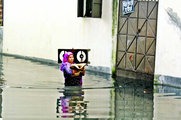 A woman is seen wading through waist deep waters to home at the capital's Basabo Bagan Bari area on Sunday as the area was inundated amid rise in the water in rivers around Dhaka.