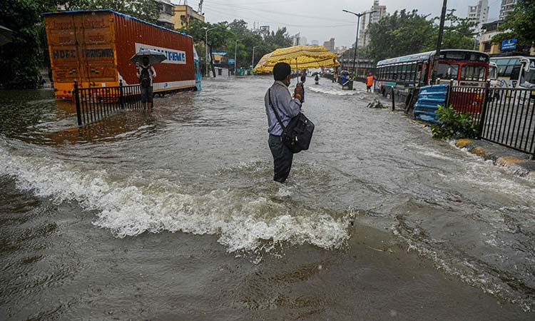 A commuter steadies himself to negotiate flowing water while crossing a flooded road in Mumbai on Tuesday.
