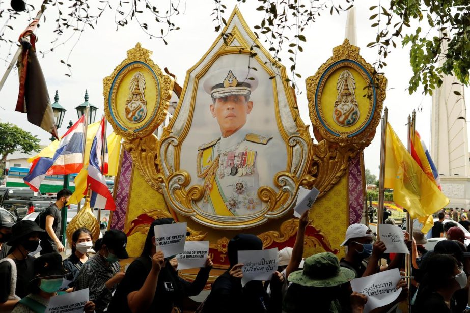 Pro-democracy protesters holding signs walk past a picture of Thai King Maha Vajiralongkorn during a rally to demand the government to resign, to dissolve the parliament and to hold new elections under a revised constitution, near the Democracy Monument i