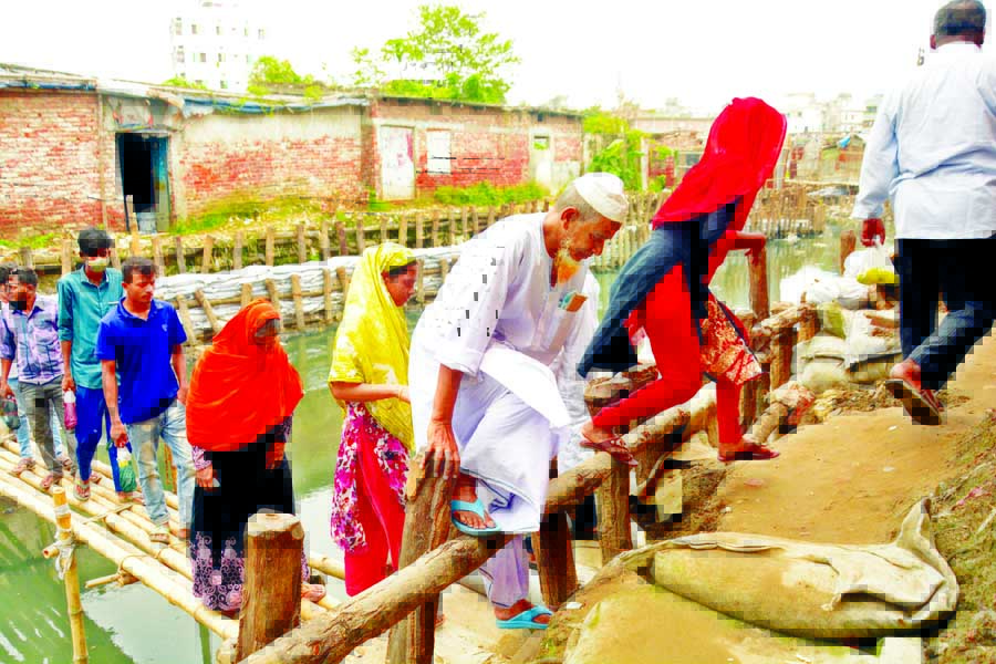 Local people are seen crossing the makeshift bamboo-made bridge on a canal at Hazaribagh in the city with serious risk of accident. The picture was taken on Wednesday.