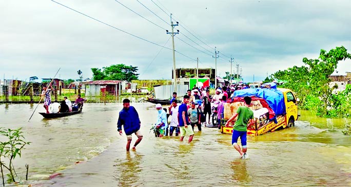 People wade through a submerged road with flood waters all around Biswambarpur upazila in Sunamganj on Friday as the Surma River was flowing 60 centimeters above danger level amid excessive rainfall in Meghalaya and Assam of India triggering flash flood i