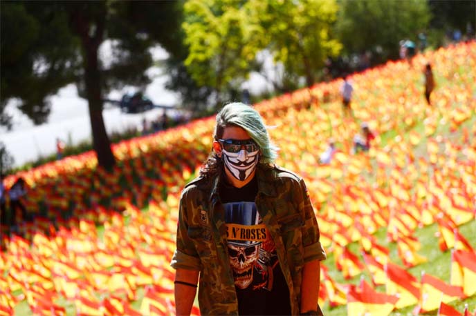 A man wearing a face mask is seen next to Spanish flags set up in memory of Covid-19 victims.