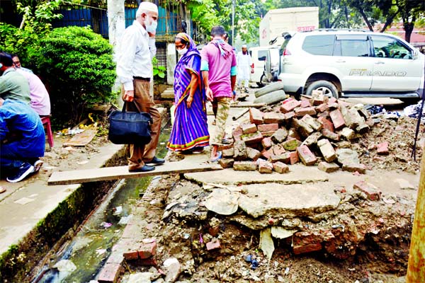 People walk through a narrow space risking their lives as construction firms piled up bricks on road after being dug out. This photo was taken from Abdul Gani Road in the capital on Thursday.