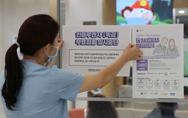 A health worker attaches a notice for suspension of influenza vaccination programmes on an entrance of a hospital in Sejong, South Korea.
