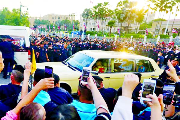 The royal motorcade carrying Thailand's Queen Suthida and Prince Dipangkorn drives past a group of anti-government demonstrators in front of Government House, on the 47th anniversary of the 1973 student uprising, in Bangkok, Thailand.