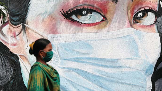 A woman walks past a graffiti of a girl wearing a protective mask amidst the spread of the coronavirus in Mumbai, India on Friday.