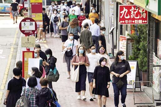 People wearing masks to protect against the coronavirus, walk down a street in Hong Kong.