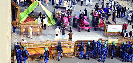 Farmers gather next to their tractors as police stand guard at a road block to stop them from marching to New Delhi to protest against the central government's recent agricultural reforms at the Delhi-Uttar Pradesh state border in Ghazipur on Tuesday.